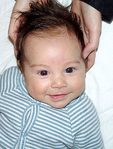 A baby boy has his head resting on a pillow, while an osteopath is treating him using cranial osteopathy with her hands under his head.